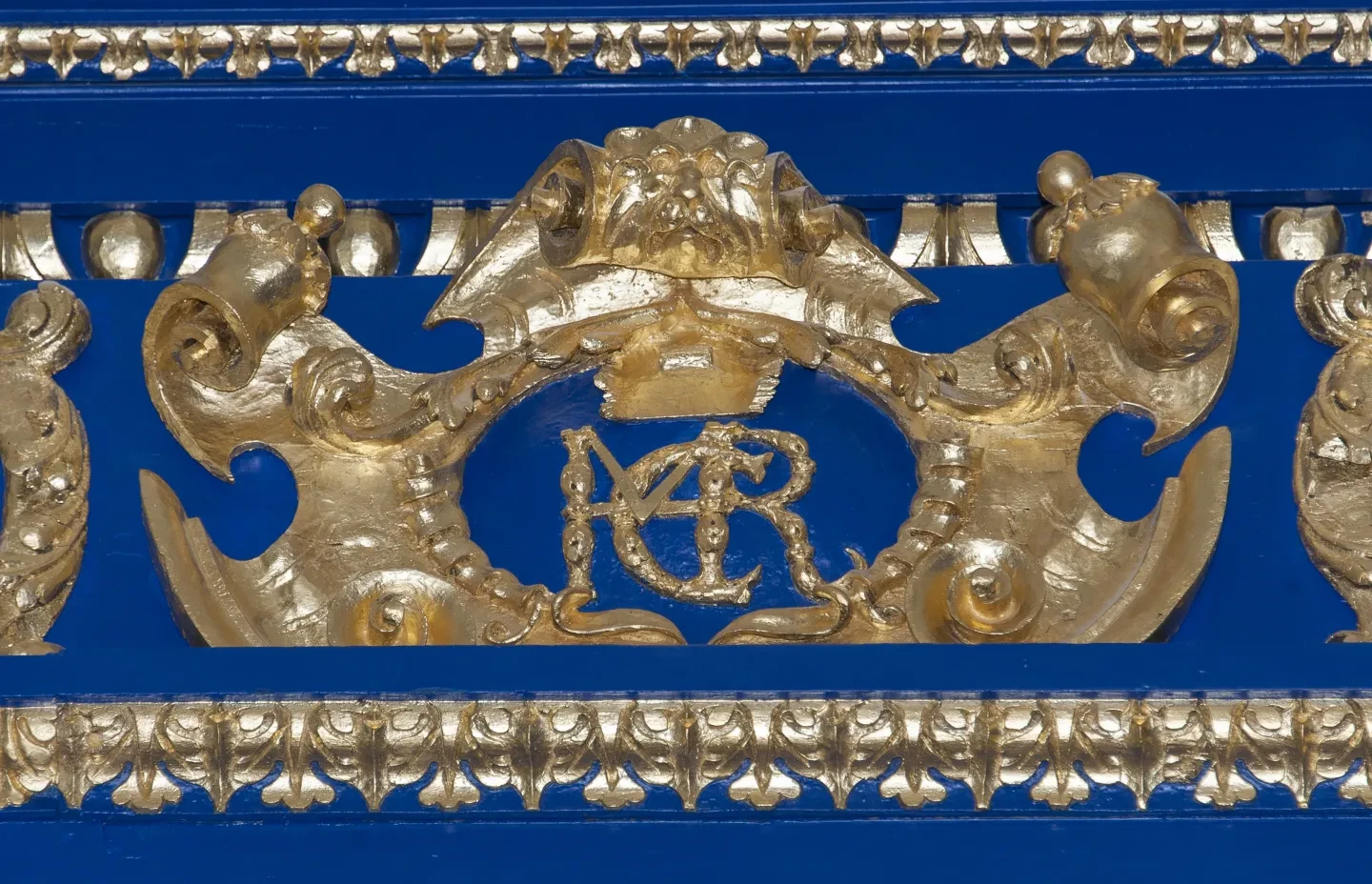 A gold cipher with the initials H M C R against a blue wall