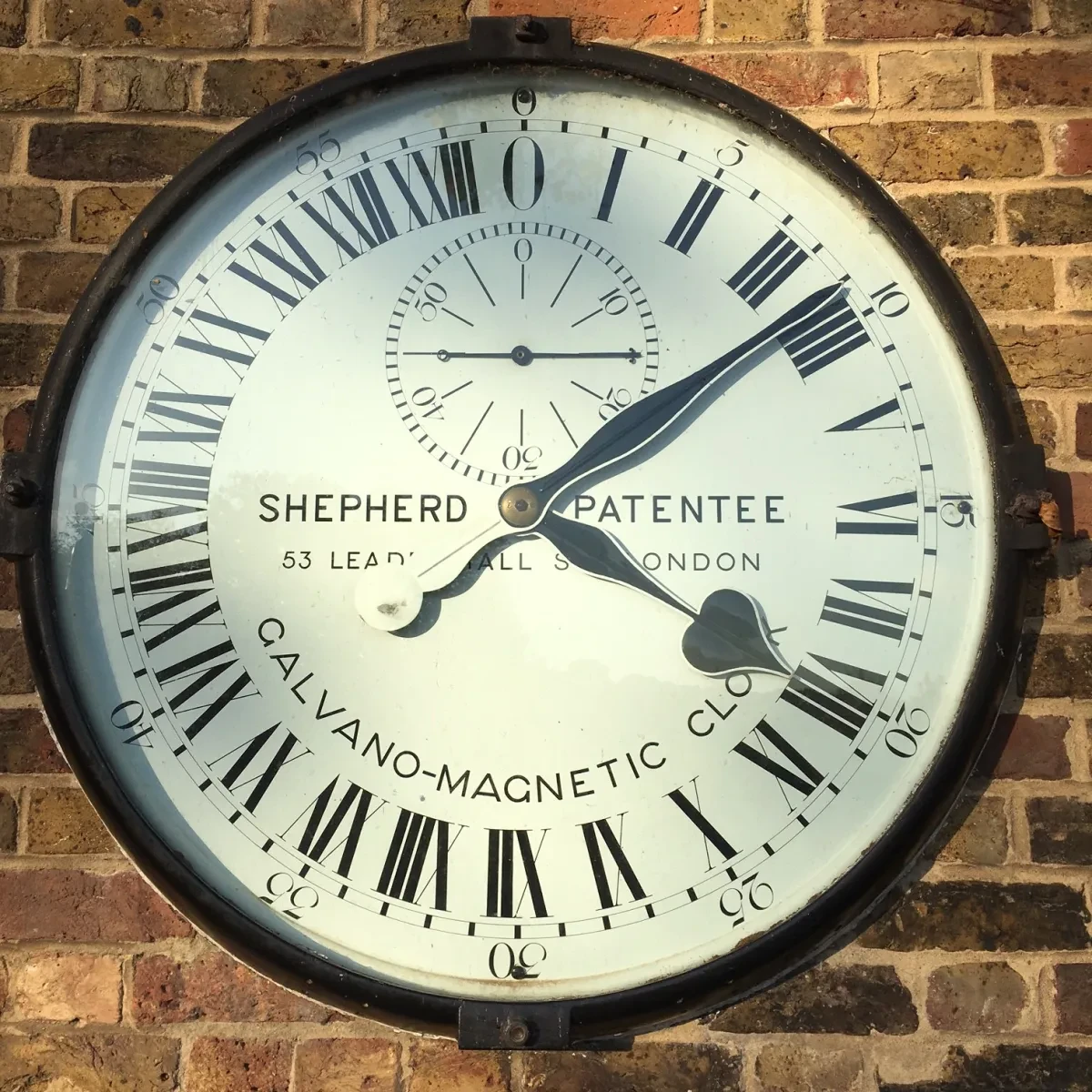 Black and white Shepherd Gate Clock on a brick wall. 