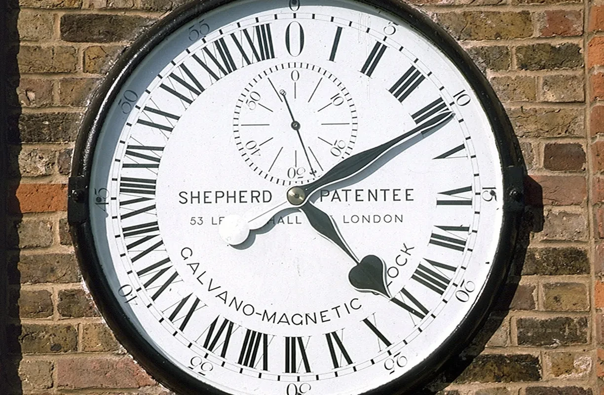 Black and white Shepherd Gate Clock on a brick wall. 