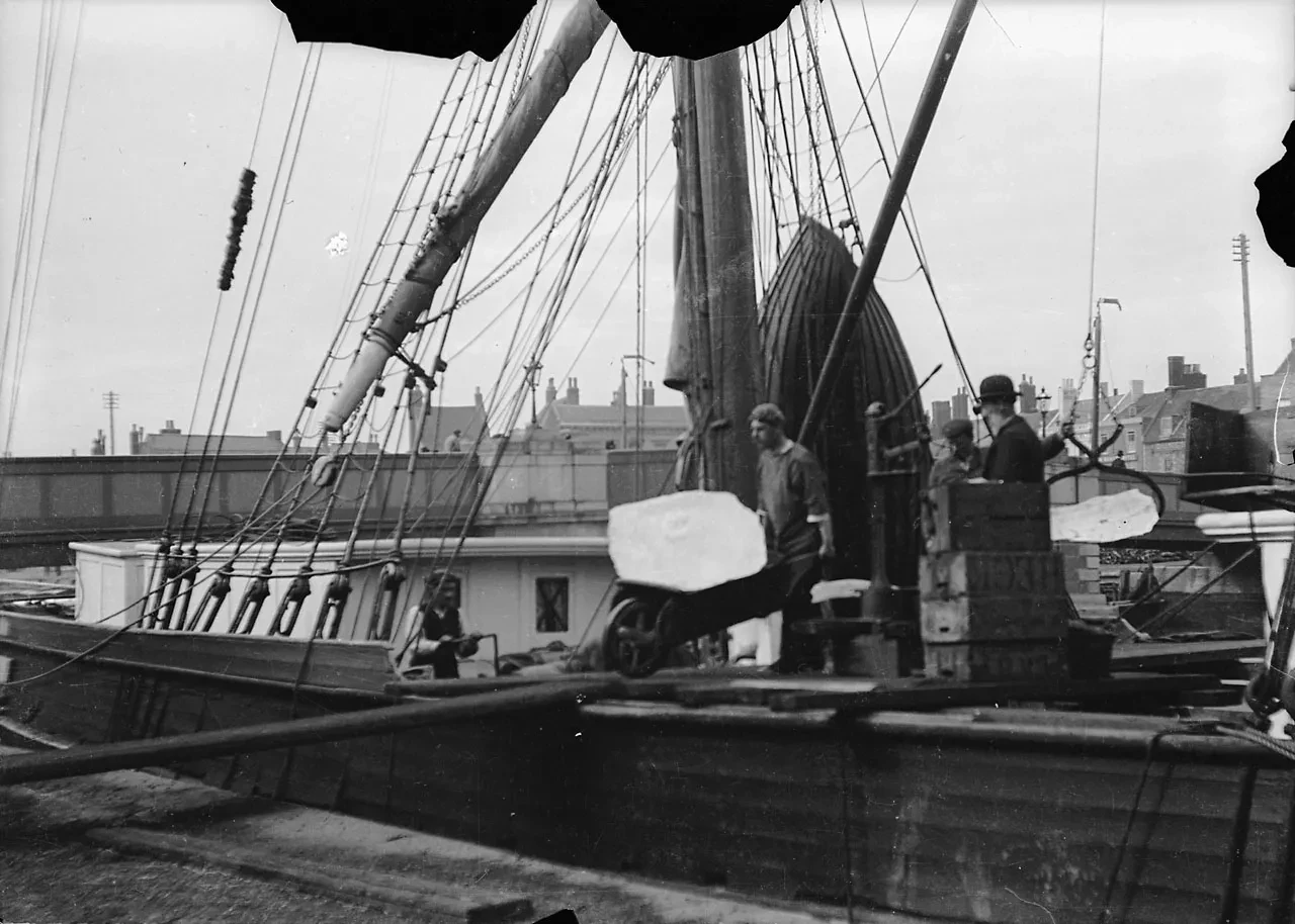 Photograph of a man transferring ice from a ship to the dock using a wheelbarrow