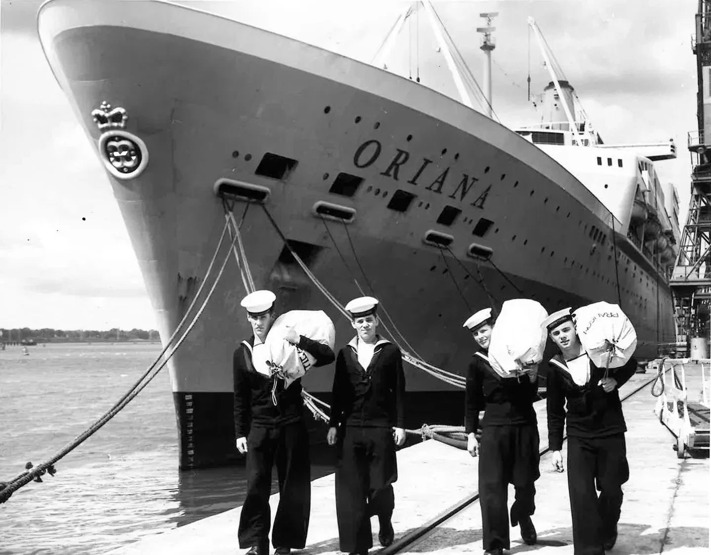 Black and white promotional image showing four Merchant Navy cadets with kit bags posing in front of the cruise liner Oriana
