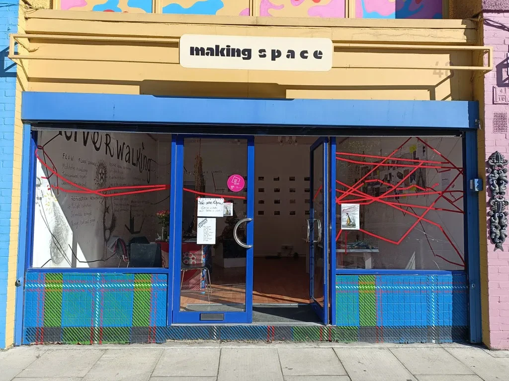 An art gallery called 'making space', with a blue shop front, open door and red lines pasted across the windows