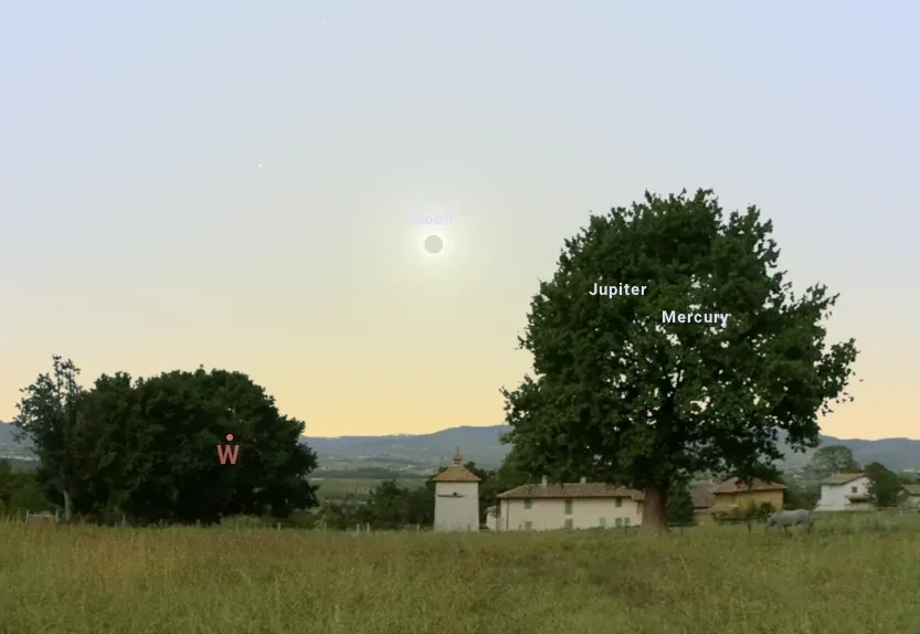 View looking west showing Moon eclipsing the Sun low in the sky, with a landscape around and the event nearly going behind a tree